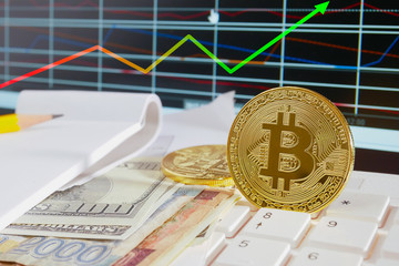 Golden bitcoin coin on placed on multiple banknotes and graphs on paper monitor exchange rates between cryptocurrency and real money