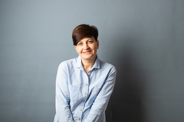 Fototapeta premium Middle-aged woman posing standing near the wall. Woman portrait on a gray background. Copy space.