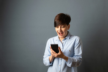 A woman holds and scans the phone, telephone conversation. Woman portrait on a gray background. Copy space.