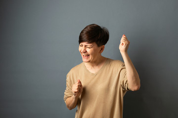A woman screams rejoices posing by the wall. Woman portrait on a gray background. Copy space.