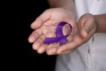 healthcare and social problem concept - womans hands holding purple domestic violence awareness ribbon