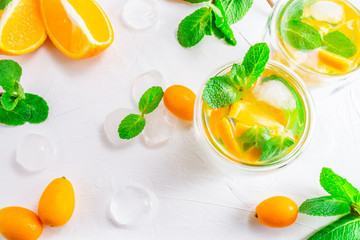 Summer citrus drink with orange, kumquat, mint and ice cubes on white background. Flat-lay, top view.