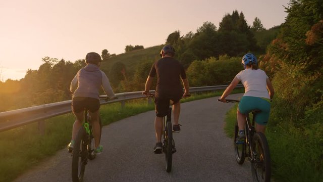 SLOW MOTION, LENS FLARE: Travelers explore the rural landscape on electric bikes at sunrise. Three friends enjoy a scenic bike trip around the picturesque countryside on an idyllic summer evening.