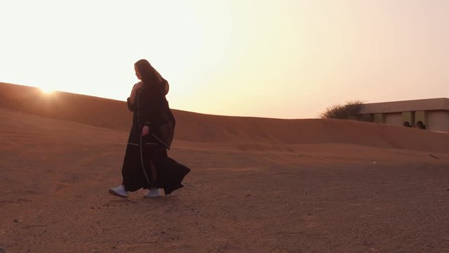 Portrait of a young Arab woman wearing traditional black clothing during beautiful sunset over the desert.