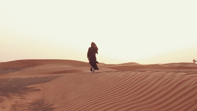 Portrait of a young Arab woman wearing traditional black clothing during beautiful sunset over the desert.