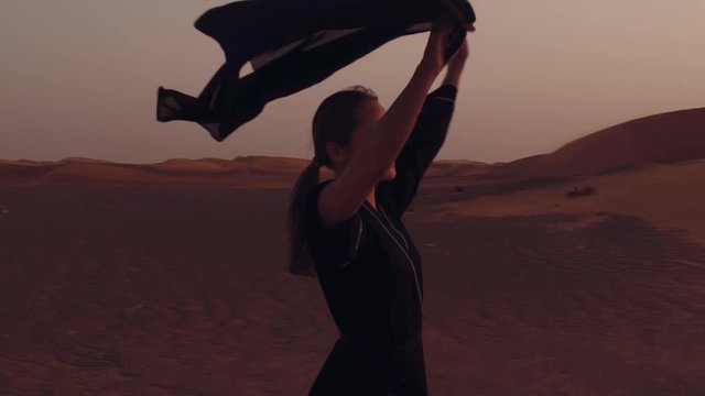 Portrait of a young Arab woman wearing traditional black clothing during beautiful sunset over the desert.