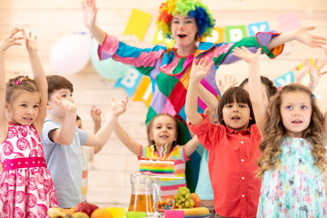 Clown playing with children. Kids group celebrate birthday and pose for camera standing with hands up at table. Holiday in a children's club.