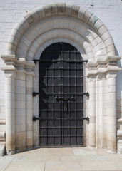 old metal gate of black color with a bolt in an arch aperture from a white stone