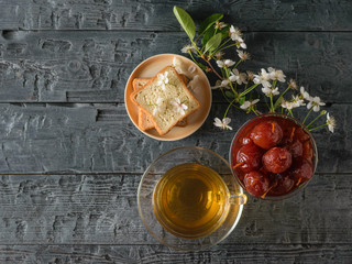 Apple jam, tea, bread and a sprig of cherry blossoms on a dark table. The view from the top. Flat lay.