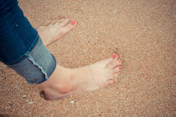 Female feet with red pedicure wear blue jean stand on the beach sand