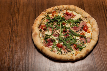 delicious whole pizza with arugula, ham, mushrooms and tomatoes