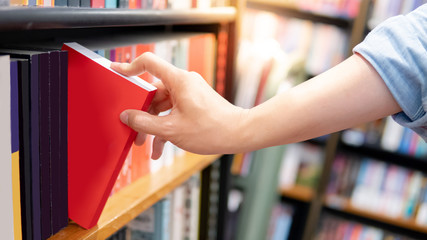 Bestseller publishing concept. Male hand choosing and picking red book from wooden bookshelf in bookstore. Education research in university public library.