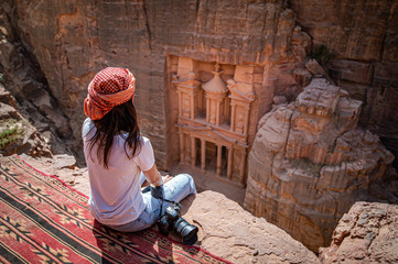 Asian woman traveler sitting on carpet viewpoint in Petra ancient city looking at the Treasury or...