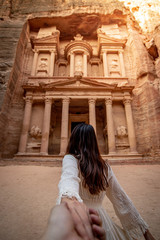 Asian woman tourist in white dress holding her couple hand at Treasury or Al-khazneh, the ancient city of Petra, Jordan. Travel UNESCO World Heritage Site in Middle East - obrazy, fototapety, plakaty