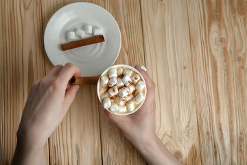 Hands holding a mug of hot chocolate or coffee with marshmallows on a dark rustic wooden table. Christmas and New year background. Top view