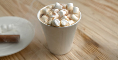 Hot morning coffee with marshmallow and cinnamon on a wooden sta