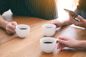 Closeup image of three people holding coffee cups to drink on wooden table