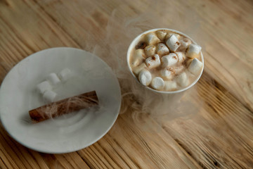 Hot morning coffee with marshmallow and cinnamon on a wooden sta