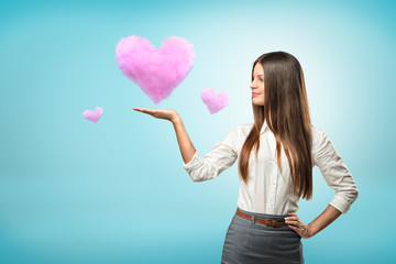 Young businesswoman holding pink cloud heart on her hand on blue background