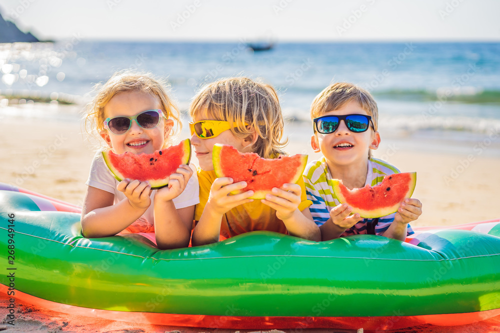 Wall mural children eat watermelon on the beach in sunglasses