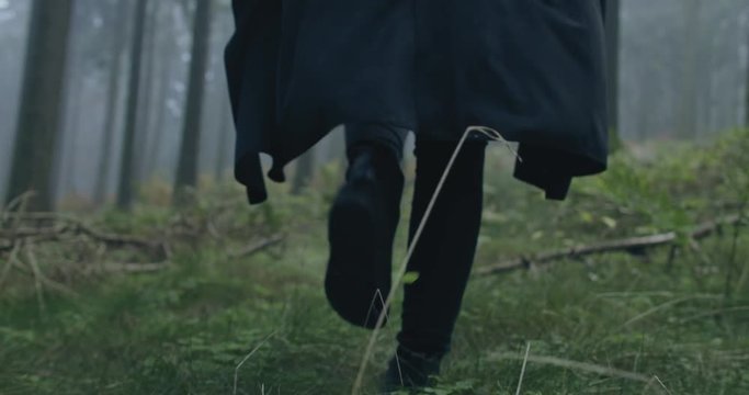 camera following a woman with black coat in forest