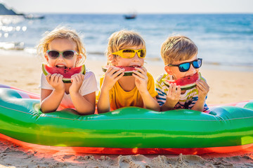 Children eat watermelon on the beach in sunglasses