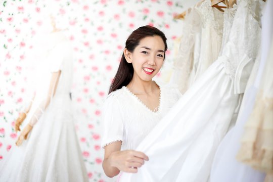 Beautiful bride getting dressed by her best friend in her wedding day and choosing a wedding dress in the shop and the shop assistant is helping her