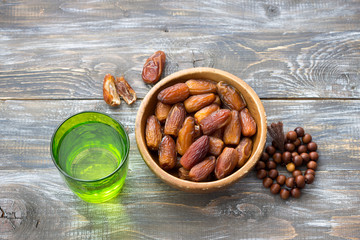 Dried dates fruits and a glass of water on a wooden table. Traditional fast breaking, Muslims...