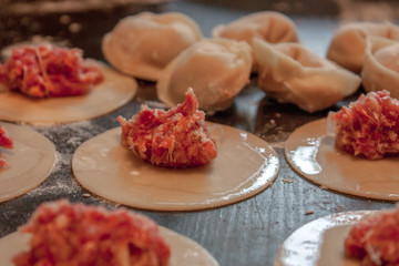 The process of making dumplings or ravioli with minced meat on a wooden table in closeup. In the background are finished products. Selective focus.