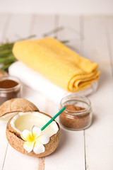 Fototapeta na wymiar Close-up of delicious fresh coconut juice with white flower and straw on wooden background with towels and chocolate body scrubs in jars