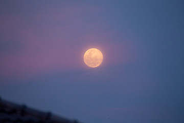 The big round moon emits beautiful light amidst the twilight sky.