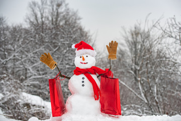 Christmas snowman on white snow background. Happy snowman with gift boxes standing in winter Christmas landscape. Snowman in a scarf and hat with shopping bag.