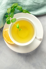 A cup of green tea with lemon and mint leaves, shot from above on an abstract grey background with copy space