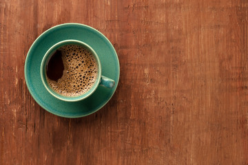 A cup of coffee on a dark rustic wooden background, shot from the top with a place for text