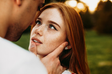 Portrait of a red haired woman with freckles and green eyes looking at her boyfriend while he is...