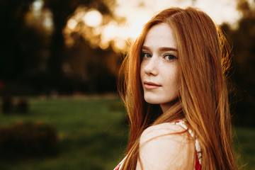 Portrait of a beautiful redhead woman with green eyes and freckles looking at camera against sunset...