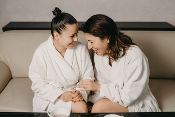 Side view portrait of two girlfriends laughing after spa massage dressed in bathrobes in a wellness spa center.
