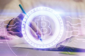 Cryptocurrency hologram, bitcoin, ico theme over hands taking notes background. Concept of blockchain. Multi exposure