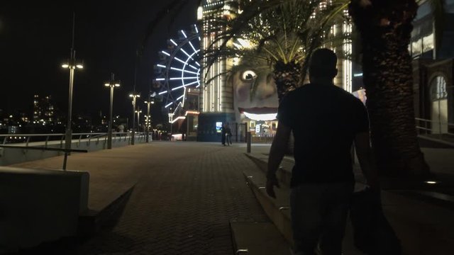 Camera Smoothly Follows Man Walking Towards Theme Park at Night