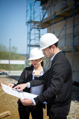 Two architects a man and a woman in construction in white helmets.