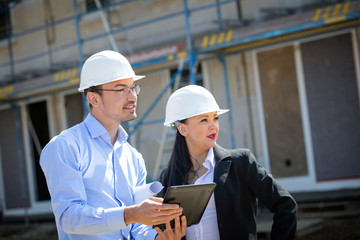 Two architects a man and a woman in construction in white helmets.