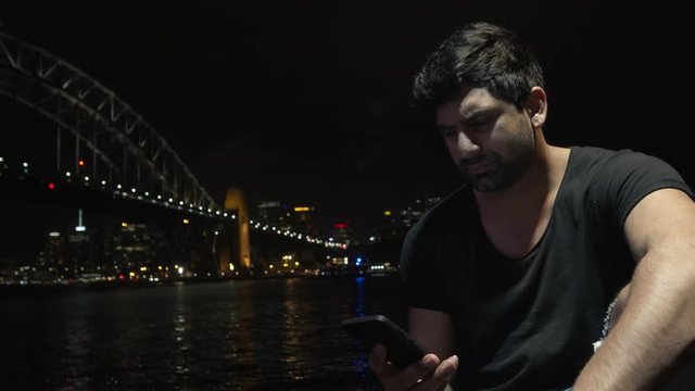 Man Sits and Looks at Sydney Night Skyline and Harbour Bridge - Takes Phone Call