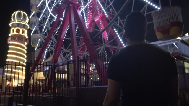 Low Angle Following Man Walking Towards Ferris Wheel in Theme Park