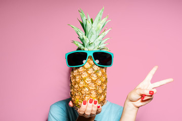 Fashion portrait woman and pineapple with sunglasses hiding head over color background