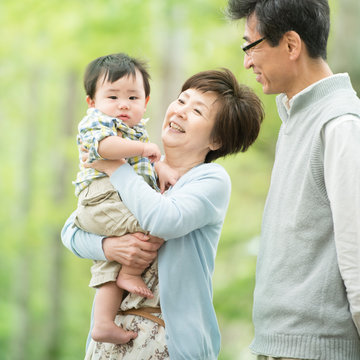 新緑の中で孫を抱き微笑む祖父母