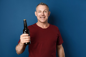 Happy middle-aged man with bottle of beer on color background