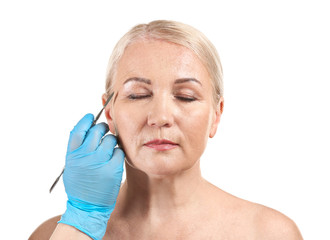 Obraz premium Mature woman and hand of plastic surgeon with lancet on white background