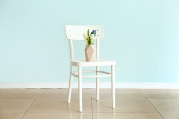 Vase with beautiful hyacinth flowers on chair against light wall