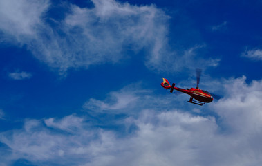 Fototapeta na wymiar Red helicopter flying with blue sky and white clouds in background