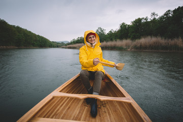 Smiling girl in yellow raincoat paddling the canoe. Rain on a wilderness canoe trip